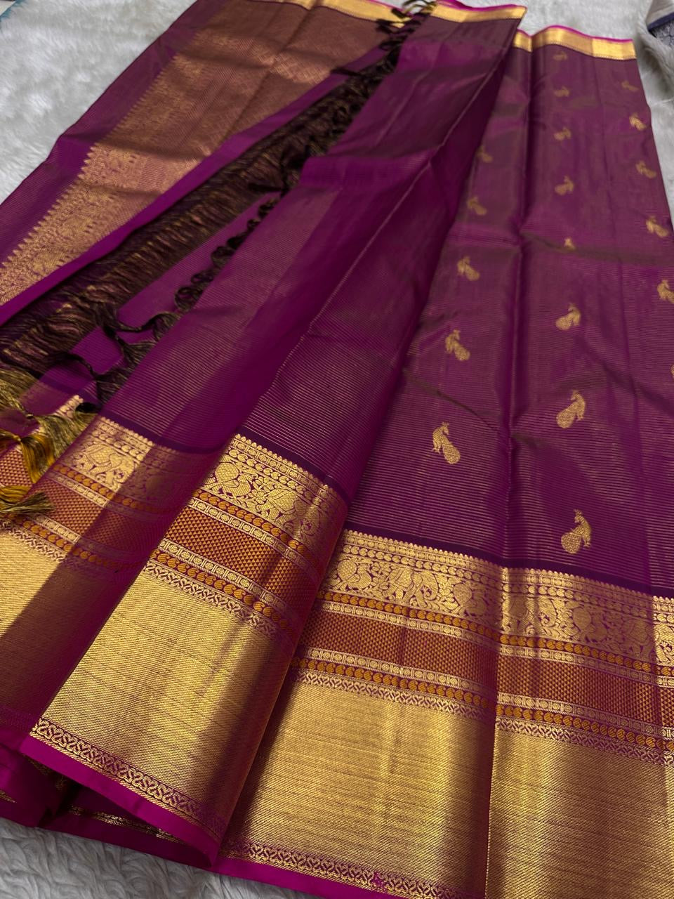Full view of magenta Kanchipuram silk saree with peacock buttas and grand gold zari borders laid out on a surface