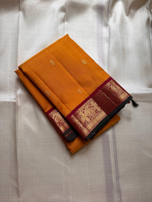 Saffron Royale – Pure Kanchipuram Silk Saree with Peacock Motif Border
Majestic saffron body with delicate zari buttas.
Rich maroon border woven with grand peacock motifs in  zari.
Traditional maroon pallu. Silk Mark Certified, delivery in 2 weeks
