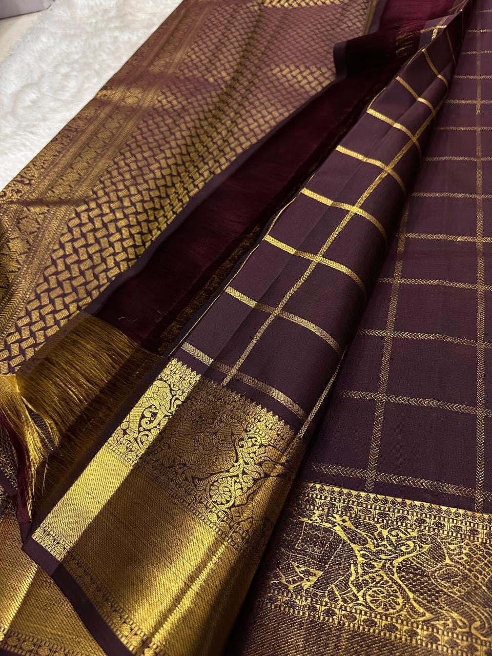 Close-up of plum Kanchipuram silk saree showing Gandaberunda zari kattam checks, intricate gold elephant border and tasselled pallu.
