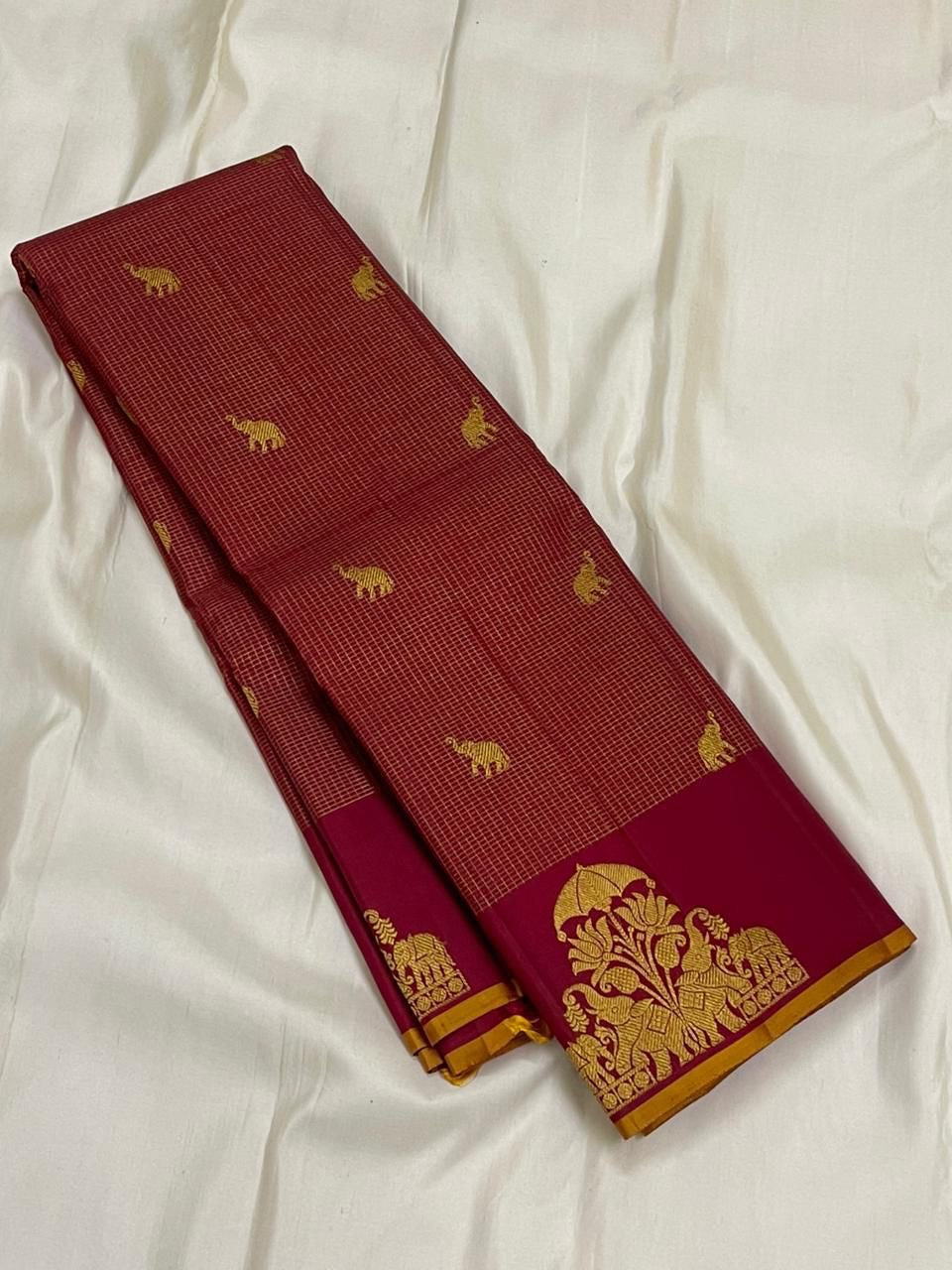 Maroon zari kattam silk saree folded lengthwise, showing gold elephant motifs and wine border with gold zari design.