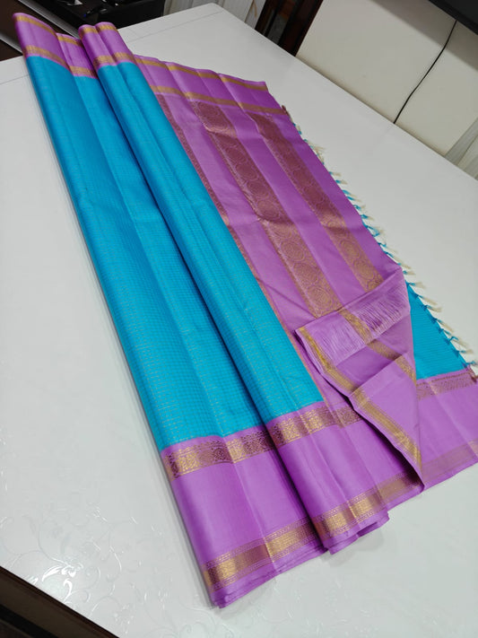Azure Kattam – Pure Silk Kanchipuram Saree
Aqua Body with Mini Checks (oosi zari  Kattam) ✨
Lilac Contrast Border in Zari Weave
Elegant Pallu with Traditional Zari Panels
Silk Mark Certified ships within  2 weeks