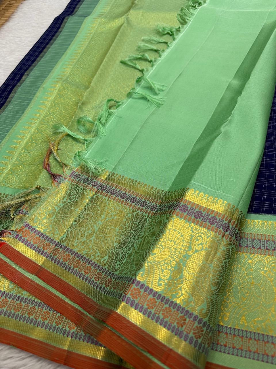 A striking blend of tradition and bold design, this navy blue Kanchipuram silk saree features delicate grid-like checks across the body. What sets it apart is the vibrant mint green and gold zari border, intricately woven with paisley and floral motifs