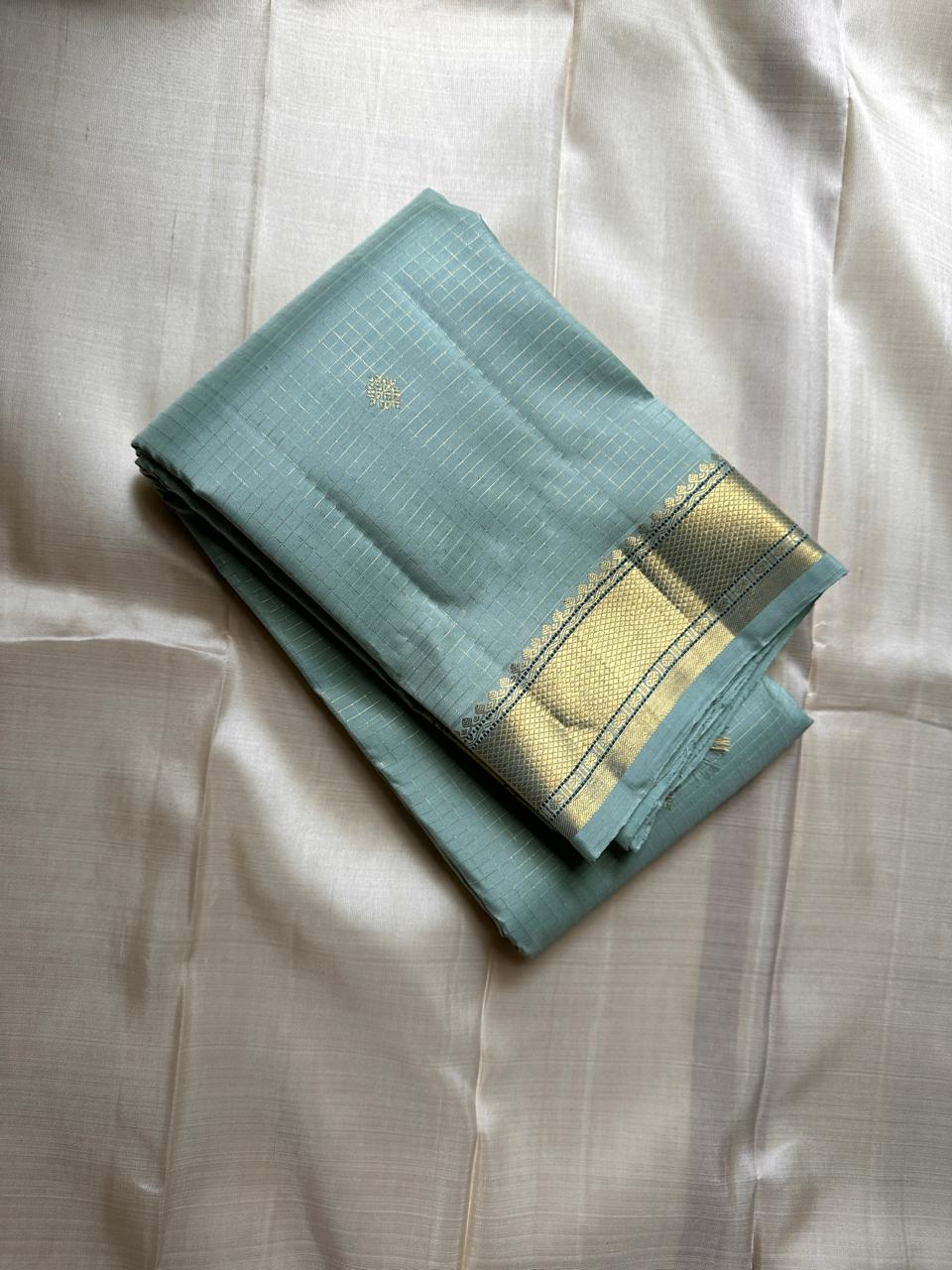 Mint Kattam – Pure Kanchipuram Silk Saree
Pastel Mint Green Body with Fine Zari Checks & Buttas
Broad Gold Zari Border with Textured Tissue Weave
Rich Gold Zari Pallu in Chevron & Striped Bands

Silk Mark Certified, delivery in 2 weeks