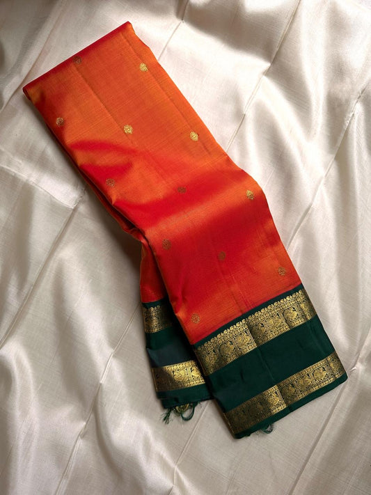 Riya – Orange Silk Saree with Dark Green Zari Border
Radiating warmth and festive charm, Riya  glows in a rich ombré of orange and vermilion, adorned with dainty gold butta motifs that shimmer gently with movement.