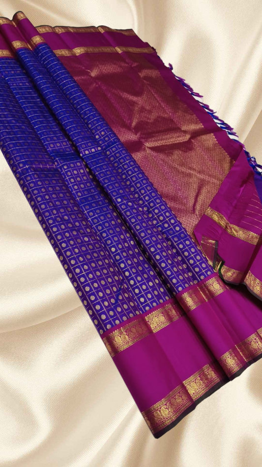 An heirloom-worthy drape woven in the finest 2G pure silk, this traditional Kanchipuram saree brings together the timeless beauty of zari buttas and checks in a rich purple body. The contrast magenta-pink rettapet border stands bold and elegant