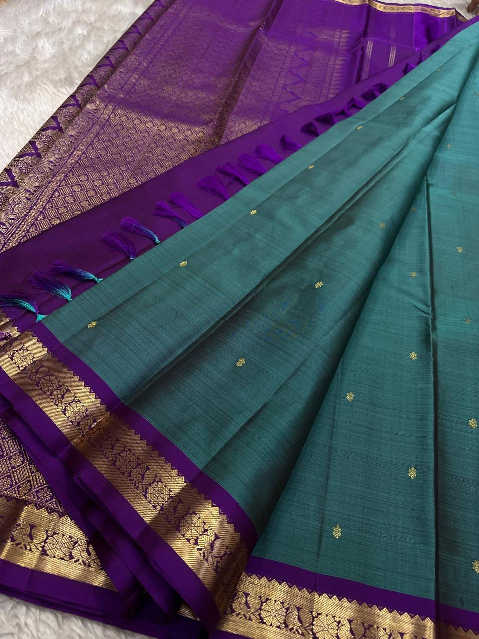 Teal pure Kanchipuram silk saree drape with purple pallu, gold zari woven work, and matching tassels.