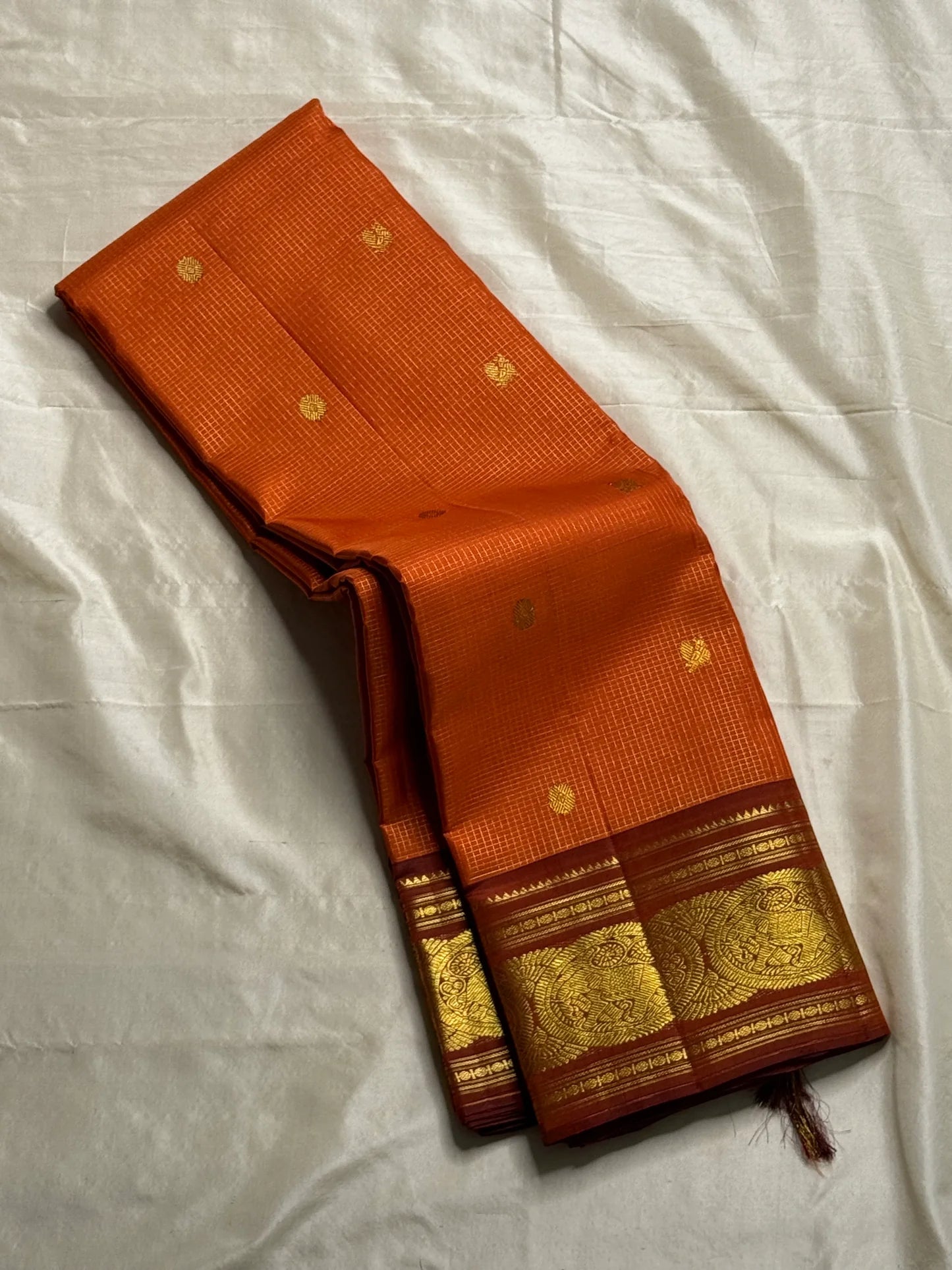 TEJAS – Vibrant Rust Orange Podi Kattam Kanchipuram Silk Saree

Micro-checks body with scattered gold chakram buttas; rich contrast maroon korvai borders

Grand circular annapakshi medallions in lustrous zari; ornate-jaal pallu & tassels

Silk Mark