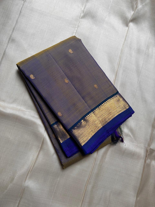 Varnam – Dove Tail Gray & Peacock Blue Kanchipuram Silk Saree. Featuring rich gold paisley buttas, a bold chevron zari border, and pure handloom silk craftsmanship ✨ Silk Mark Certified | Blouse Stitching Available | Free USA Shipping