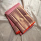 Rose Twilight — Kanchipuram Pure Silk

 Soft blush-pink (gulabi) body with gold floral buttas

Rosé-gold zari borders with floral vines & creepers

Vermilion-orange contrast pallu with kaddi & brocade panels

Silk Mark Certified | Free Shipping within USA