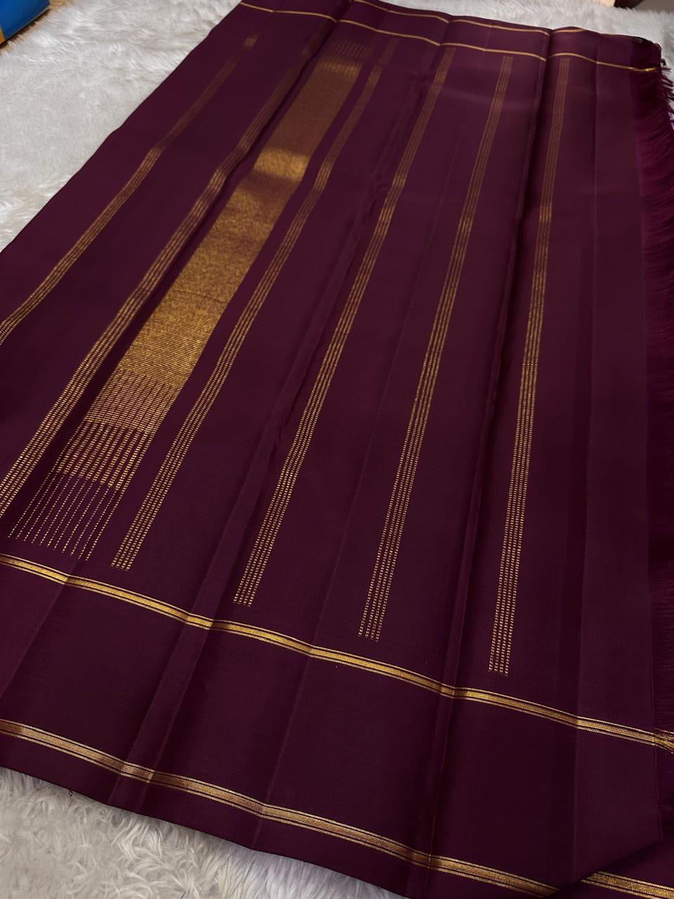 Ilam  Vadamalli Chakram — Kanchipuram Pure Silk

Pastel lilac–mauve body with gold & silver chakram buttas

Deep plum contrast border with twin kaddi zari lines

Plum pallu with elegant vertical zari stripes; lilac tassels

Silk Mark Certified •