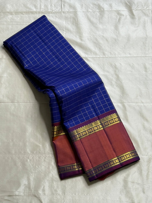 Indra Neelam Kattam – Pure Kanchipuram Silk Saree
Royal Blue Body with Fine Zari Grid Checks
Copper-Rose Korvai Borders with Floral & Chevron Zari
Grand Purple Pallu with Tassels
Silk Mark Certified | ships in 2  weeks | Blouse Stitching Available