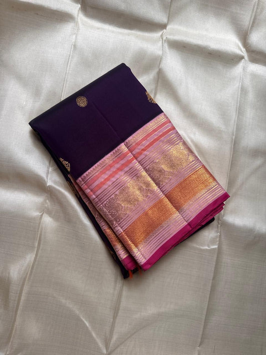 Shyamala—named after the deep, dark shade it embodies 💜 A pure Kanchipuram silk masterpiece with a rich purple body sprinkled with golden zari buttas. The contrast pink border glows with floral and paisley zari motifs, accented in coral and rose-gold, wh