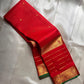 Partly opened red Kanchipuram silk saree showing fine pinstripes with small gold buttas and gold-lined border with green edge.