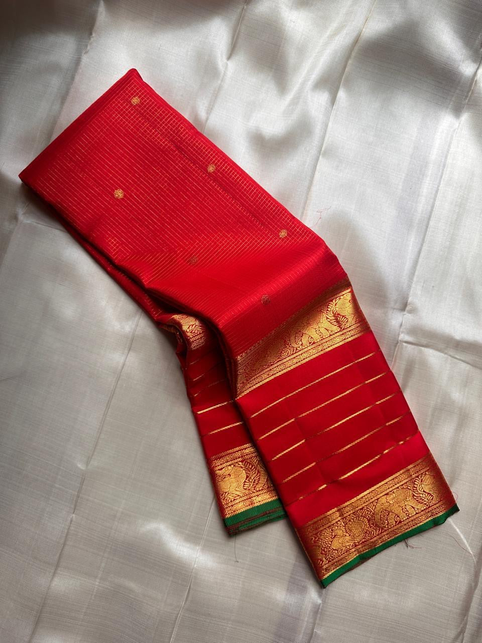 Partly opened red Kanchipuram silk saree showing fine pinstripes with small gold buttas and gold-lined border with green edge.