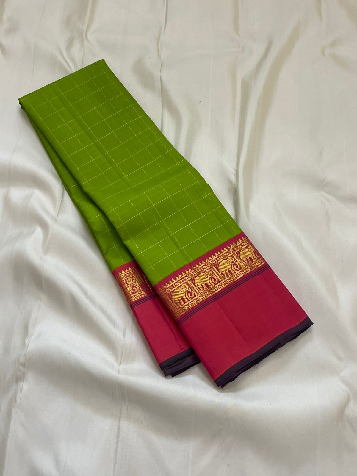 Valli Pachai – Kanchipuram Pure Silk Saree

Parrot-green body in kattam (grid) checks with subtle zari lines

Korvai contrast rani-pink borders featuring gaja (elephant) procession & temple reku motifs

Rich rani-pink zari pallu with vertical bands