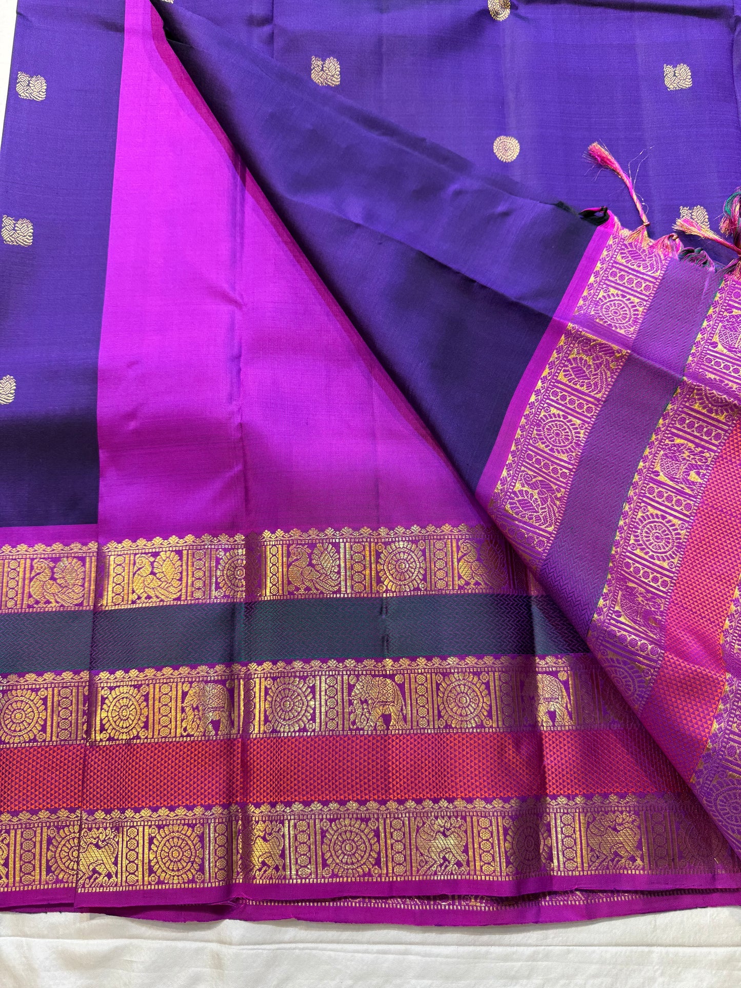 Peacock Purple Rajam – Pure Silk Kanchipuram Saree
Deep Peacock Purple Body with Gold Zari Buttas
Korvai Borders with Temple, Peacock & Elephant Motifs
Rich Zari Pallu with Vertical Brocade Stripes
Silk Mark Certified | ships in two week| Blouse Stitching