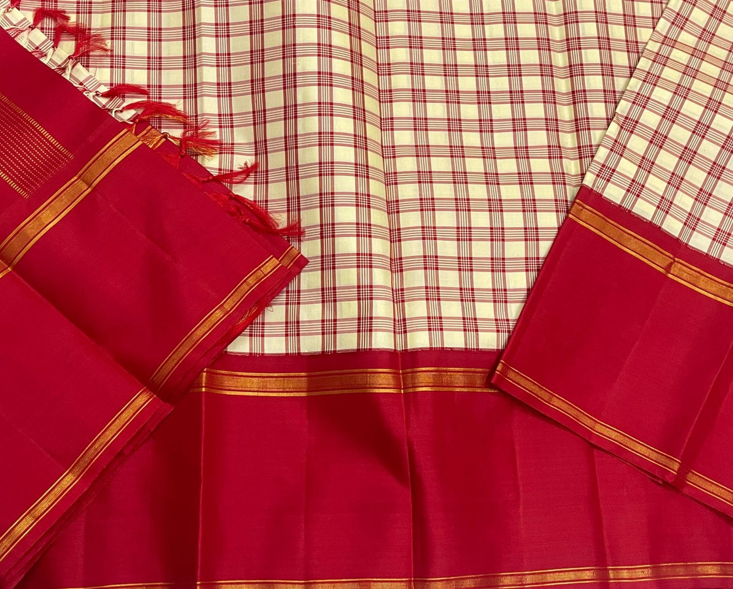 Close-up of cream and red checked section with deep red border and thin gold zari woven lines, with red tassels visible.