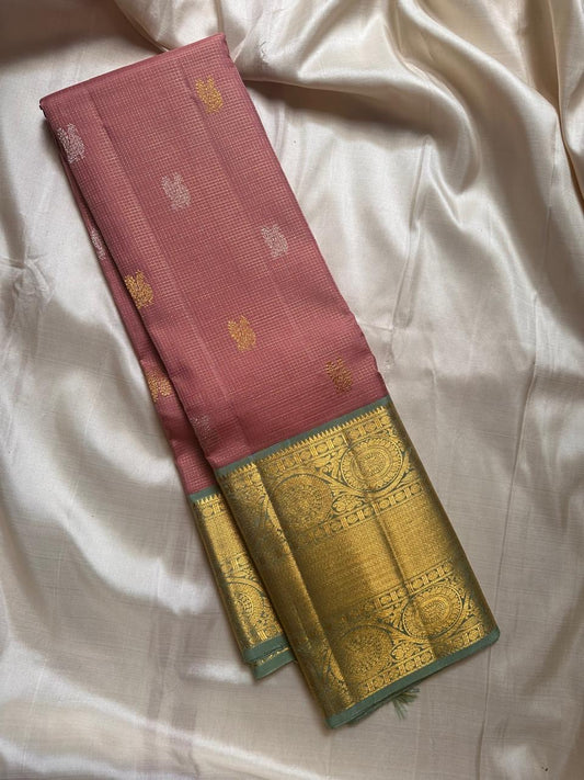 Vahini – Pleasant Peach Pink Pure Kanchipuram Silk Saree with Zari Kattam Checks, Silver & Gold Peacock Buttas, Sage Green Border Adorned with Kamalam Vines and Baavanji Motifs, and an Ornate Zari Pallu with Majestic Peacocks