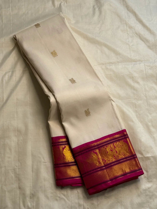 Ivory silk saree laid out with small gold buttas and a fuchsia gold-zari border, shown on a white sheet.