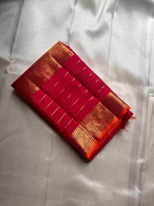 Folded pink-red Kanchipuram silk saree with gold zari lines and rich elephant border on an ivory silk background.