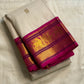 Folded ivory silk saree with fuchsia border and gold zari woven panels, photographed on a white fabric background.