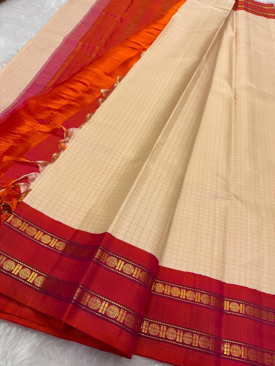 Sharvani Red– Cream Checked Silk Saree with Red Orange shot color Zari Border & Vibrant Pallu
A timeless silk saree featuring a cream body with delicate red checks, complemented by a striking red zari border pallu.