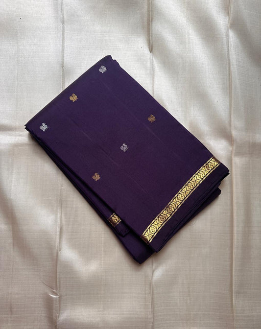Folded deep purple Kanchipuram silk saree with small gold and silver buttas and slim diamond zari border on an ivory background.