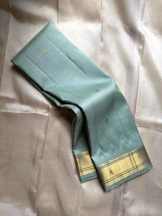 Mint Kattam – Pure Kanchipuram Silk Saree
Pastel Mint Green Body with Fine Zari Checks & Buttas
Broad Gold Zari Border with Textured Tissue Weave
Rich Gold Zari Pallu in Chevron & Striped Bands

Silk Mark Certified, delivery in 2 weeks