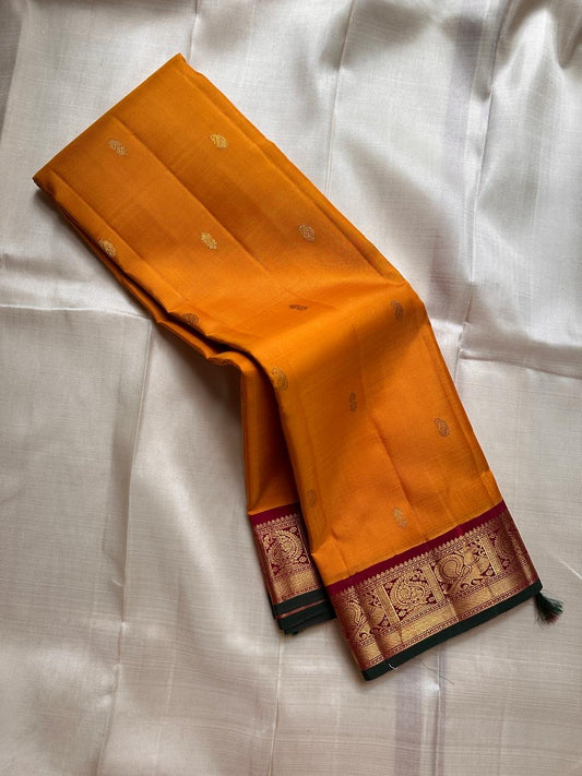 Saffron Royale – Pure Kanchipuram Silk Saree with Peacock Motif Border
Majestic saffron body with delicate zari buttas.
Rich maroon border woven with grand peacock motifs in  zari.
Traditional maroon pallu. Silk Mark Certified, delivery in 2 weeks