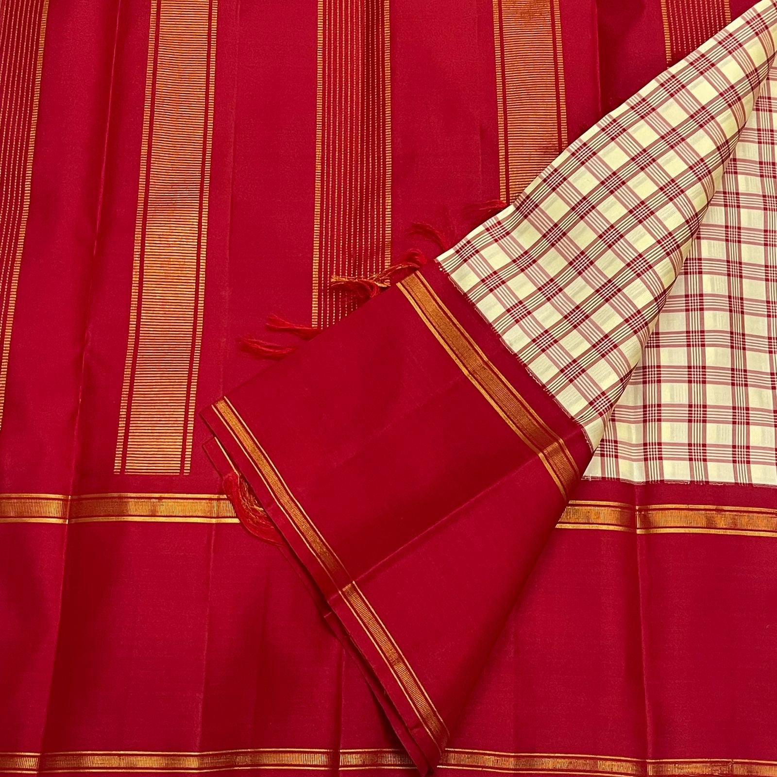 Red silk pallu laid flat with vertical gold zari woven stripes, with the checked cream section and red border folded on top.
