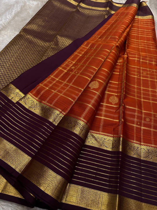 Cinnamon Kattam – Pure Kanchipuram Silk Saree
Vermillion red body with gold kattam checks & floral  buttas
Contrast plum purple korvai borders with rich zari weave
Grand zari pallu with lattice & floral motifs in gold
Silk Mark Certified ships in 2weeks