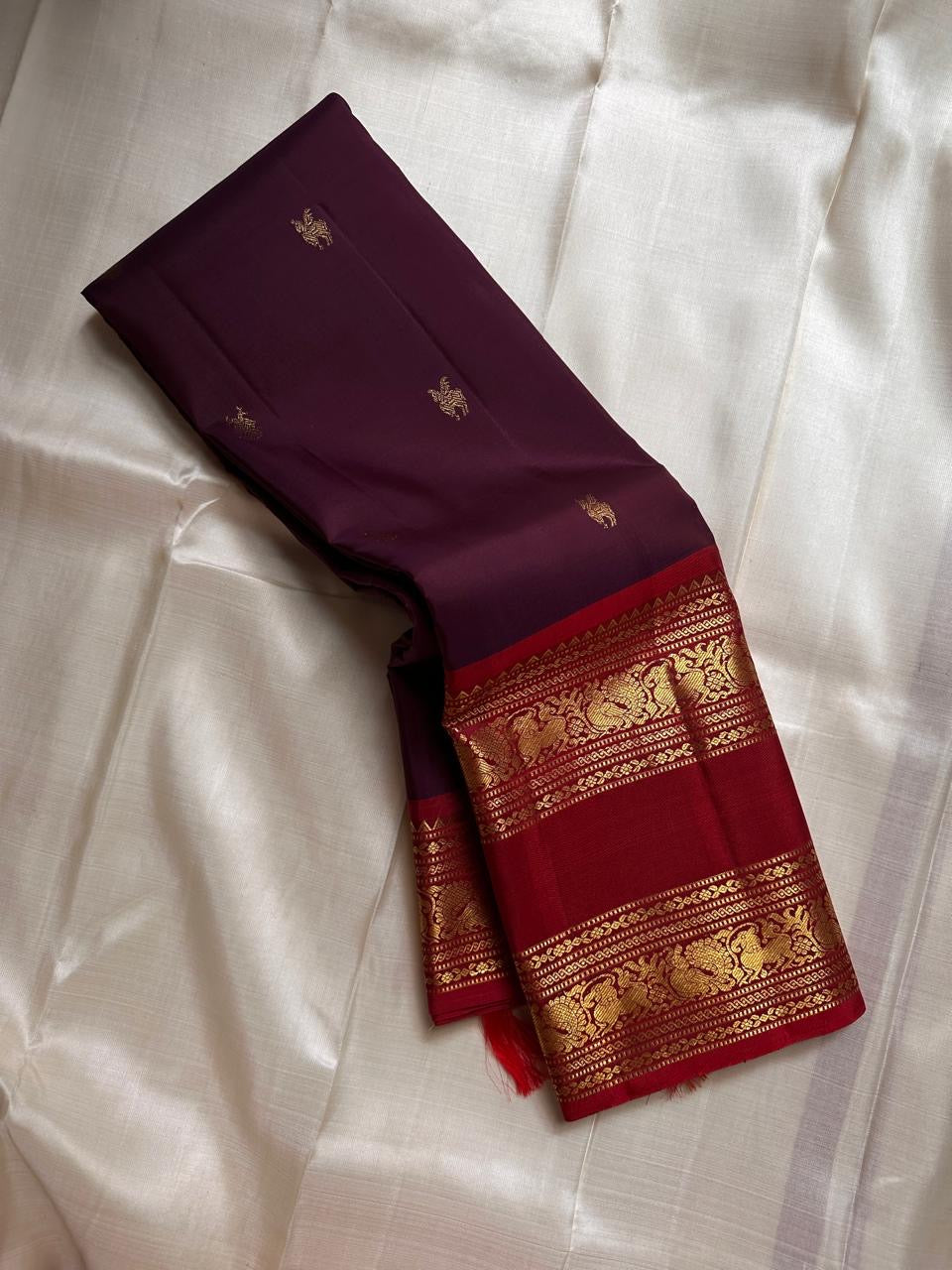 Purnima ✨ – Kumkum-Red & Aubergine Kanchipuram Pure Silk Saree
With Zari Winged Horse Buttas on the Aubergine Body
Grand Gold Annam & Floral Korvai Border with Temple Rekku
Varisaipettu Striped Gold Brocade Pallu with Hand-Knotted Tassels
Silk Mark