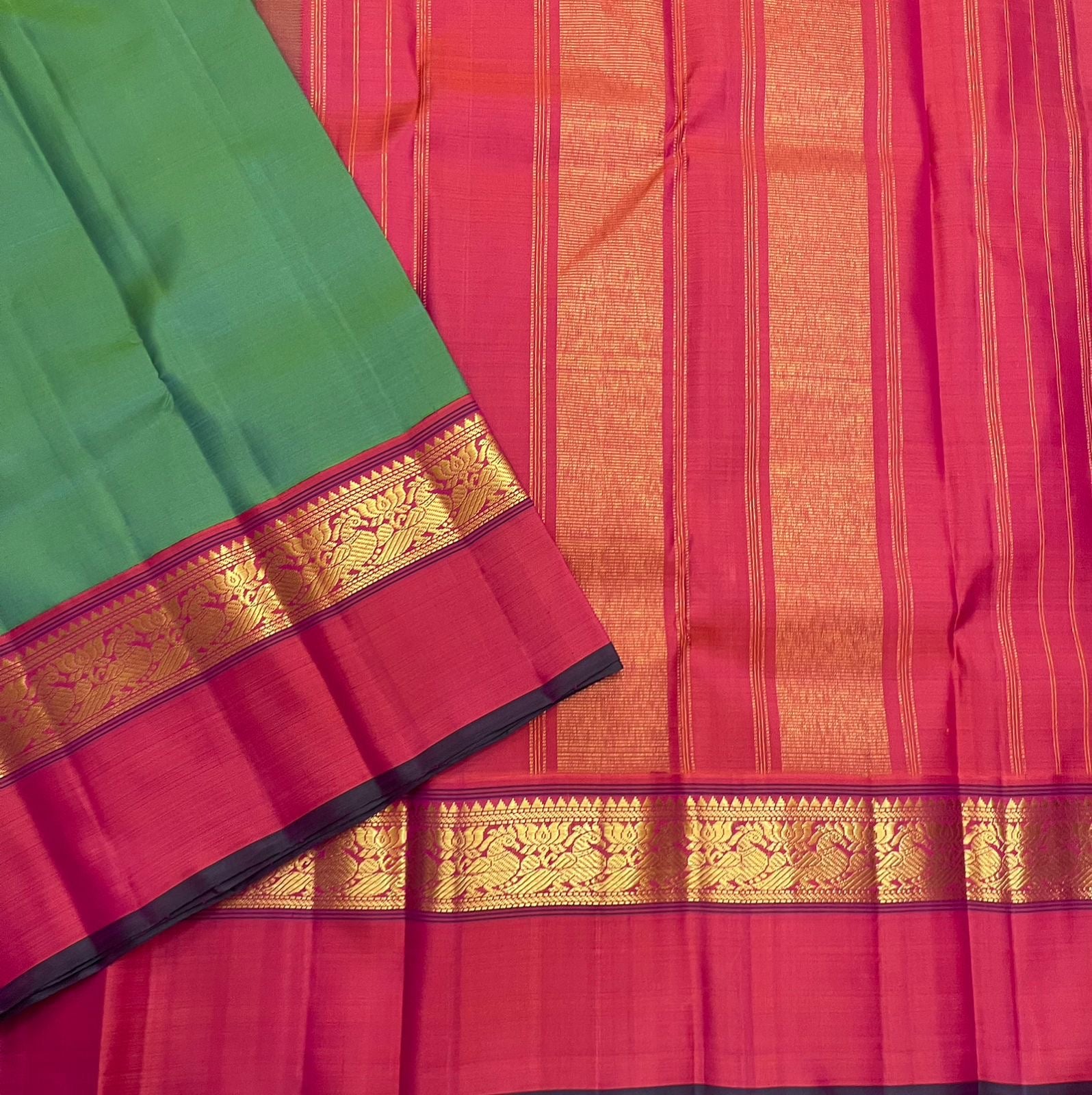 Green saree with pink border and gold zari woven band laid over a pink pallu with vertical zari stripes and gold panels.