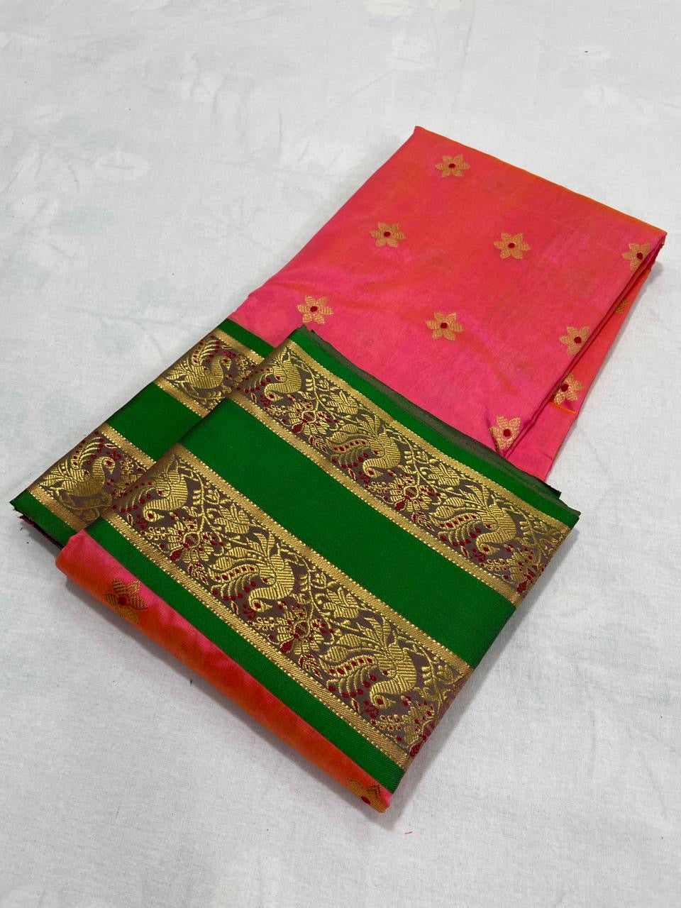 Folded Coral Pink Pattu Silk Chanderi saree with gold floral buttas and emerald green border