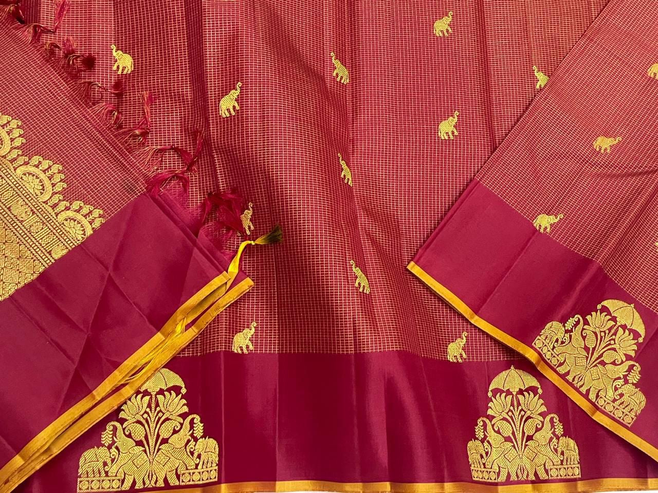 Draped maroon zari kattam saree showing tassels, gold elephant motifs, and wine border with large thiruvizha motif.