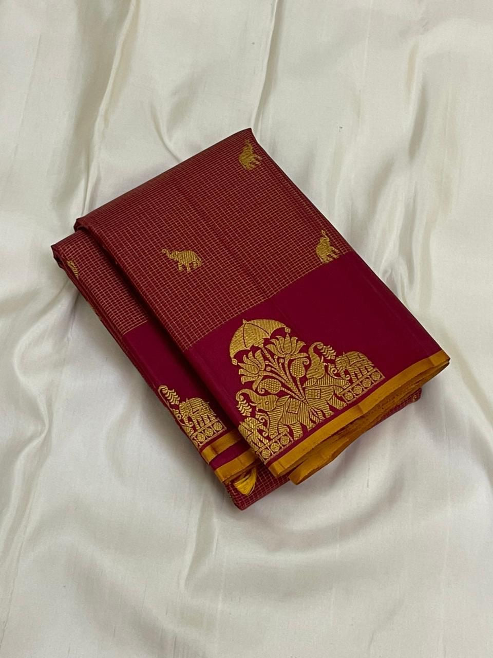 Folded maroon vairaoosi zari kattam Kanchipuram silk saree with gold elephant buttas and wine border on white fabric.