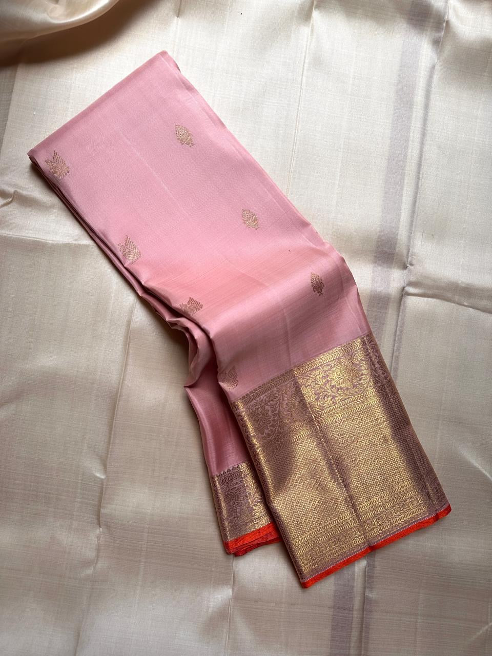 Rose Twilight — Kanchipuram Pure Silk

 Soft blush-pink (gulabi) body with gold floral buttas

Rosé-gold zari borders with floral vines & creepers

Vermilion-orange contrast pallu with kaddi & brocade panels

Silk Mark Certified | Free Shipping within USA