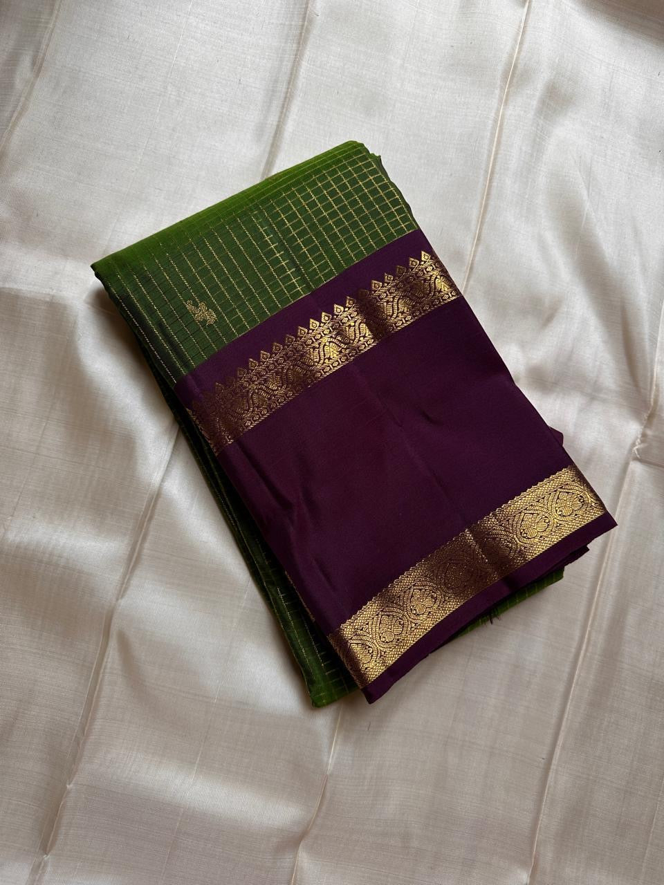 Iravati – Earthy Green Kanchipuram Pure Silk Saree
A graceful weave in a rare earthy green tone, adorned with gold zari kattam and butta.
Accented by a rich plum rettapet border with delicate flower vine motifs.
