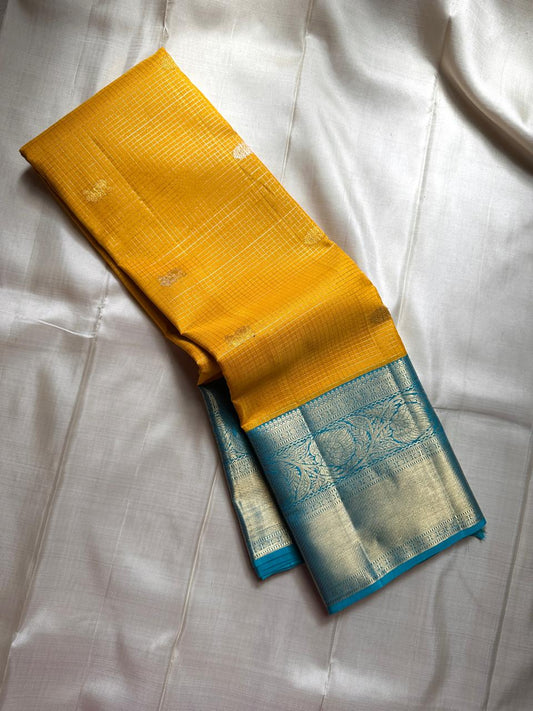 This radiant yellow pure silk drape is elevated by an exquisite and unexpected pairing — a serene sky blue border, making it both eye-catching and rare. Fine zari checks shimmer gently across the body, timeless bavaanji border