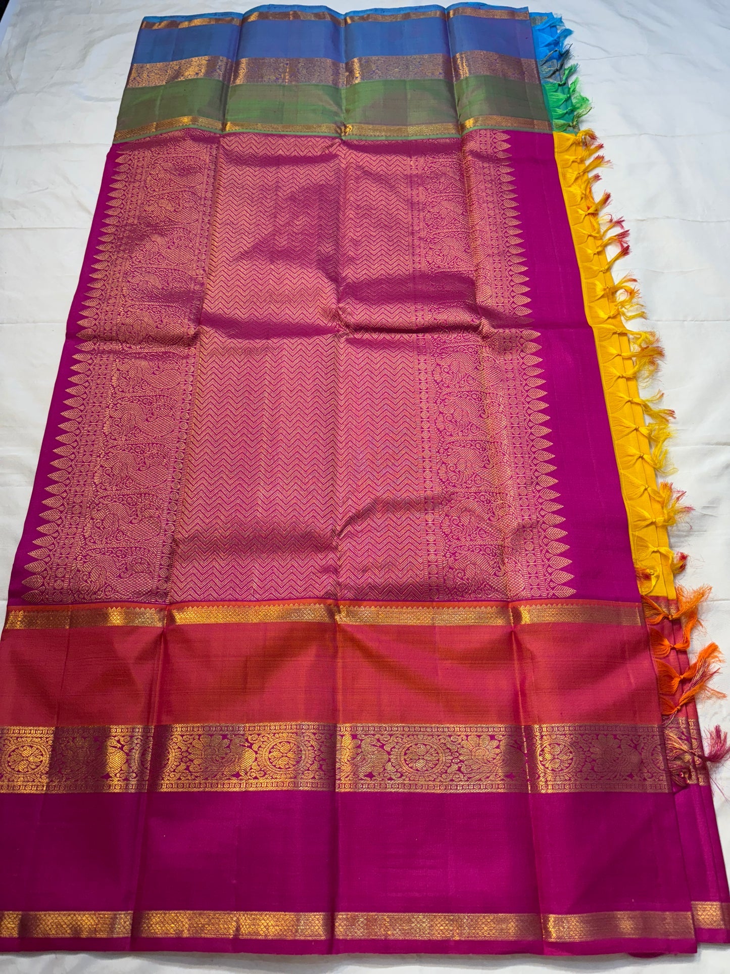 Varna Jaalam — Kanchipuram Pure Silk

Manjal yellow body with gold chakram buttas

Rani pink korvai border with floral & coin zari panels

Magenta–orange chevron pallu with blue–green color block top

Silk Mark Certified • Free Shipping within USA •