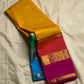 Varna Jaalam — Kanchipuram Pure Silk

Manjal yellow body with gold chakram buttas

Rani pink korvai border with floral & coin zari panels

Magenta–orange chevron pallu with blue–green color block top

Silk Mark Certified • Free Shipping within USA •