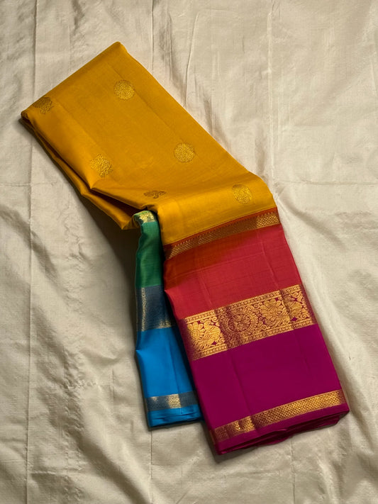 Varna Jaalam — Kanchipuram Pure Silk

Manjal yellow body with gold chakram buttas

Rani pink korvai border with floral & coin zari panels

Magenta–orange chevron pallu with blue–green color block top

Silk Mark Certified • Free Shipping within USA •