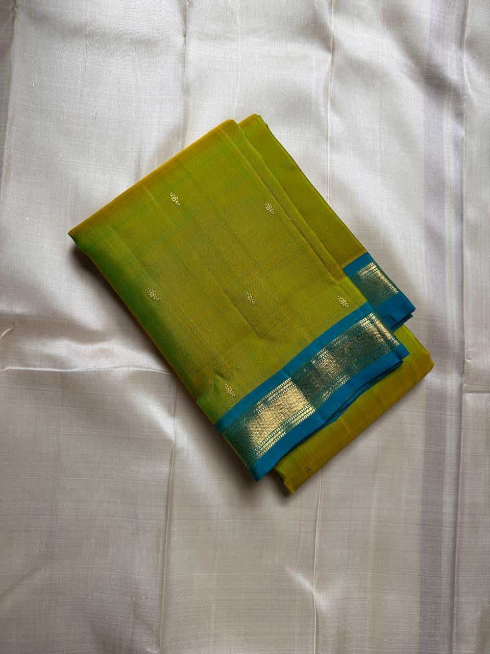 Citrus and Teal – Pure Kanchipuram Silk Saree
Dual-tone body in parrot green and turmeric.
Elegant gold leaf buttas across the drape.
Teal korvai border
Rich teal pallu with diamond jaal and temple motifs.

Silk Mark Certified, delivery in 2 weeks
