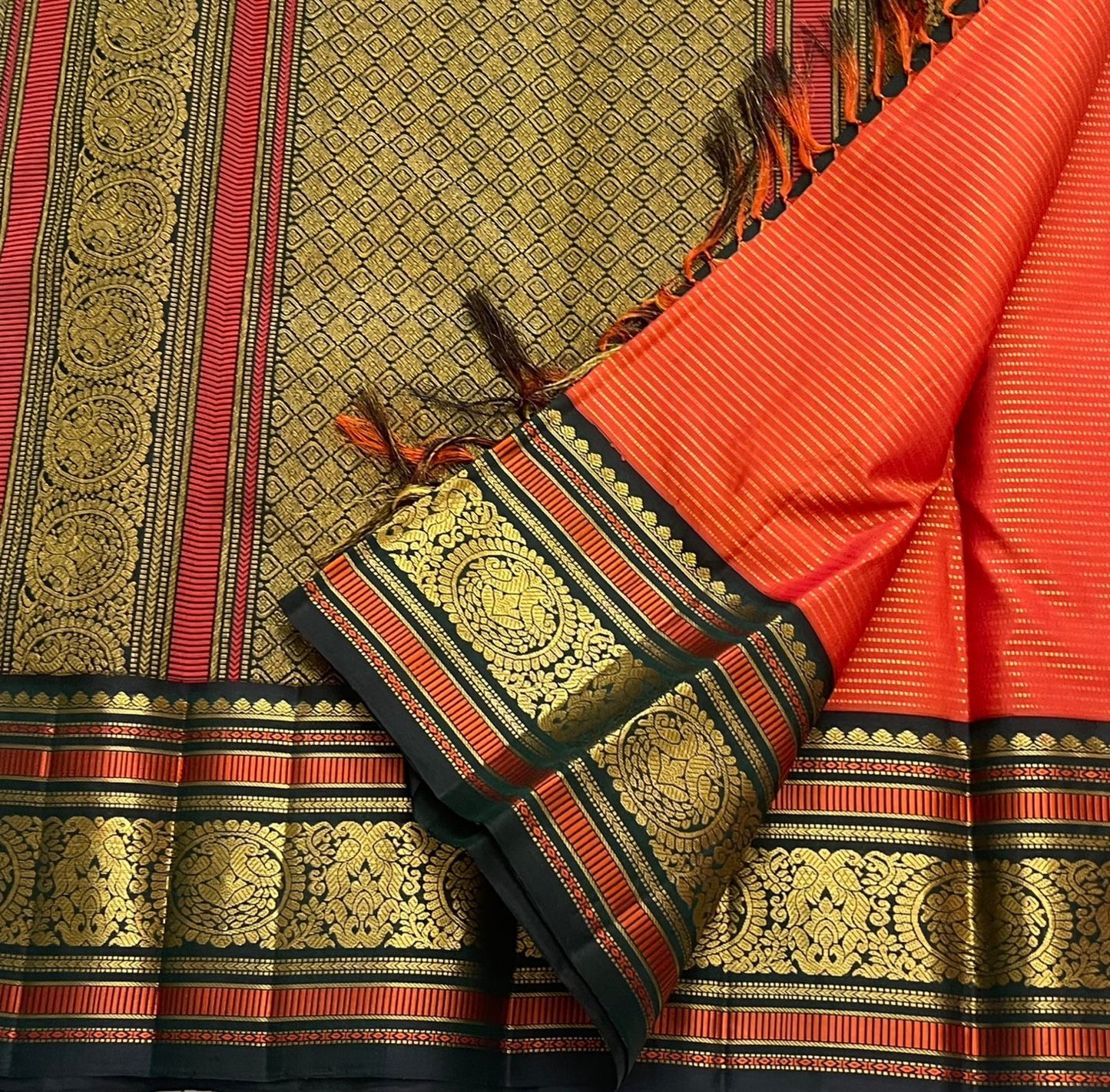 Aruna Mayil Chakram
Pure Kanchipuram Silk Saree – Reddish-Orange Body with Gold Zari Chakram Buttas
Contrast Bottle Green Korvai Borders with Mayil & Temple Motifs
Grand Zari Pallu with Diamond Brocade Weave & Hand-Knotted Tassels
Silk Mark Certified ✅ |