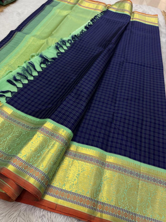 A striking blend of tradition and bold design, this navy blue Kanchipuram silk saree features delicate grid-like checks across the body. What sets it apart is the vibrant mint green and gold zari border, intricately woven with paisley and floral motifs