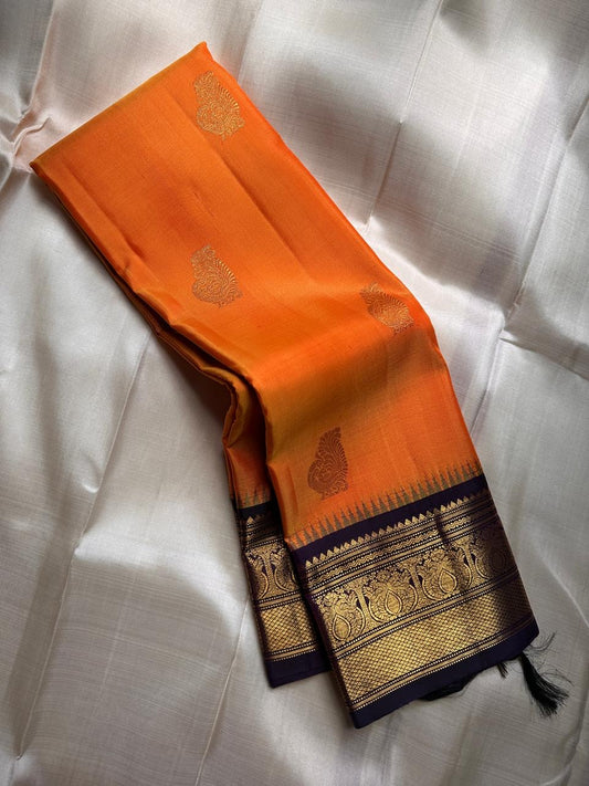 Pure Kanchipuram Silk Saree – Saffron-Orange Body with Gold Zari Paisley Buttas
Contrast Deep Purple Korvai Borders with Intricate Temple & Floral Motifs
Grand Purple Zari Pallu with Diagonal zariWeave . Silk mark , ships in 2 weeks