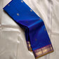 Sapphire Orchid celebrates the classic blue–purple pairing of Kanchi. The body is a rich sapphire/cobalt blue with tiny floral buttas in gold zari. A striking amethyst-purple korvai border and grid pavun Zari pallu Silk Mark Certified, delivery in 2 weeks