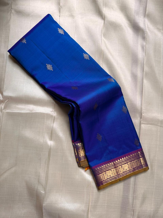 Sapphire Orchid celebrates the classic blue–purple pairing of Kanchi. The body is a rich sapphire/cobalt blue with tiny floral buttas in gold zari. A striking amethyst-purple korvai border and grid pavun Zari pallu Silk Mark Certified, delivery in 2 weeks