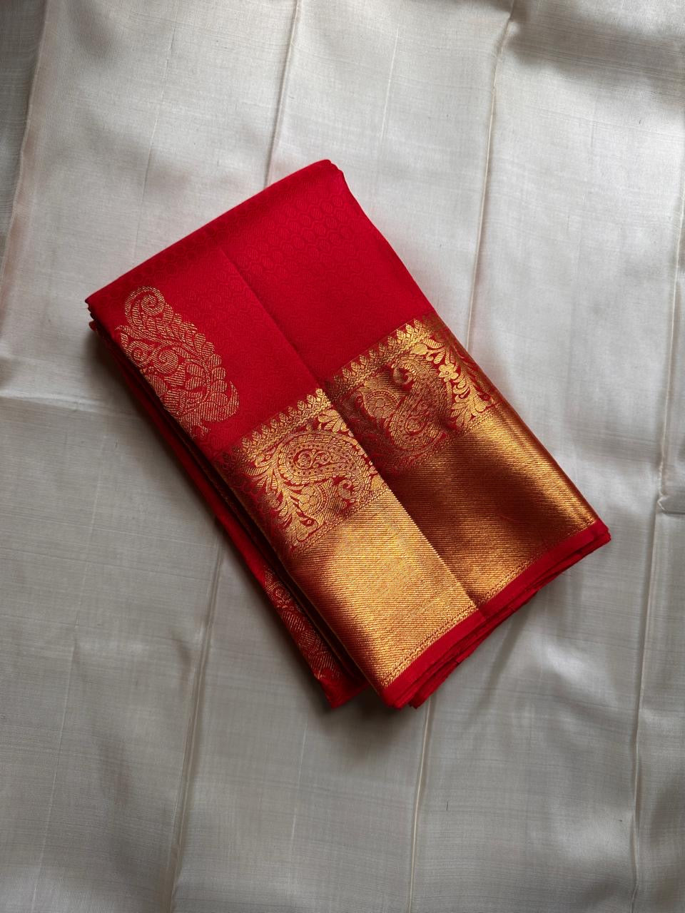 A traditional Kanjivaram (Kanchipuram) silk saree, vibrant red orange peacock floral motifs bavanji border and ornate grid motif Pallu