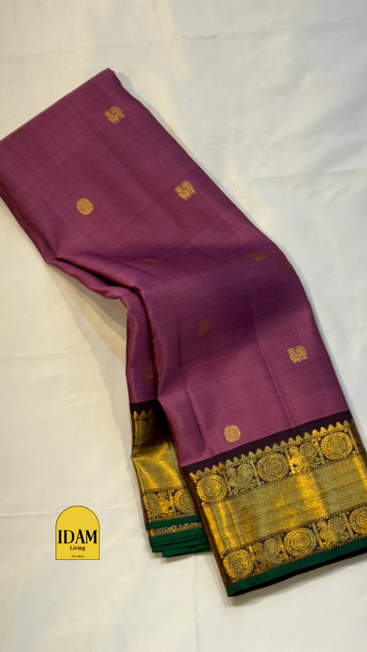 Tanaya features a regal mulberry mauve purple body adorned with golden kamalam and mayil buttas. Its elegant dual-tone border—coffee brown on top and emerald green below with rich temple-inspired zari work with medallions and florals woven, rich Pallu.